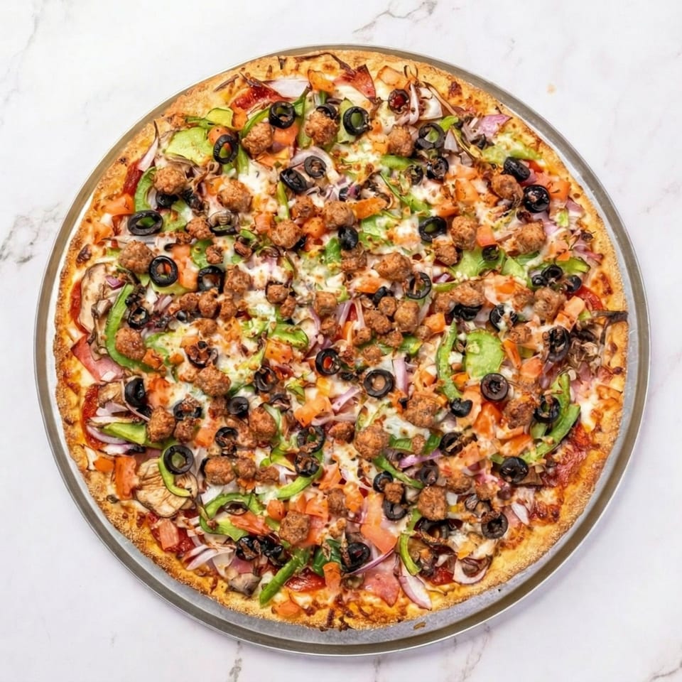 A large, fully loaded pizza with sausage, olives, peppers, onions, and tomatoes on a metal tray.