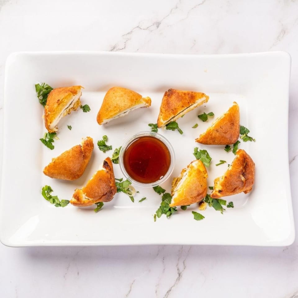Golden-brown fried dumplings, some cut open, with a side of red dipping sauce and cilantro garnish.