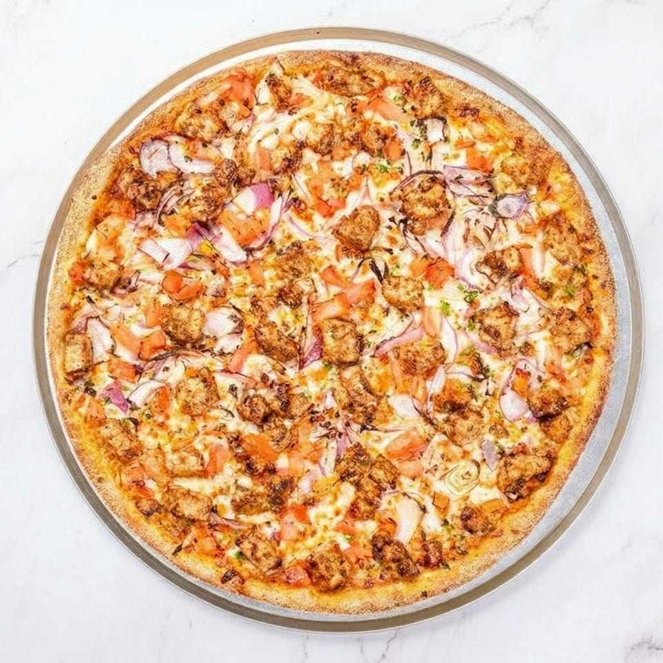 A whole chicken pizza with red onions and tomatoes on a metal pan.